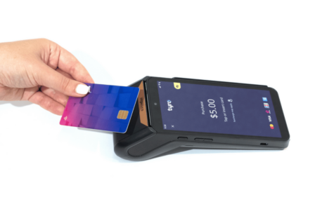 A person holding a credit card to a mobile phone for payment using a Tyro EFTPOS machine.