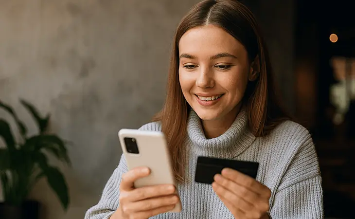 Person smiling looking at phone and credit card