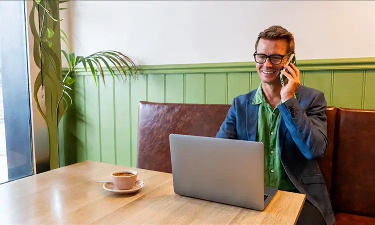 Man on phone in front of laptop in cafe