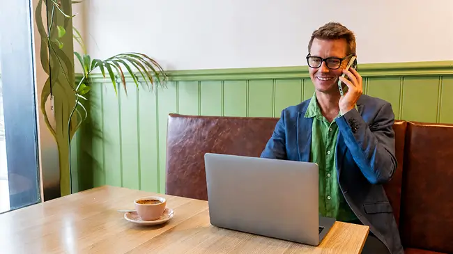 Man on phone in front of laptop in cafe