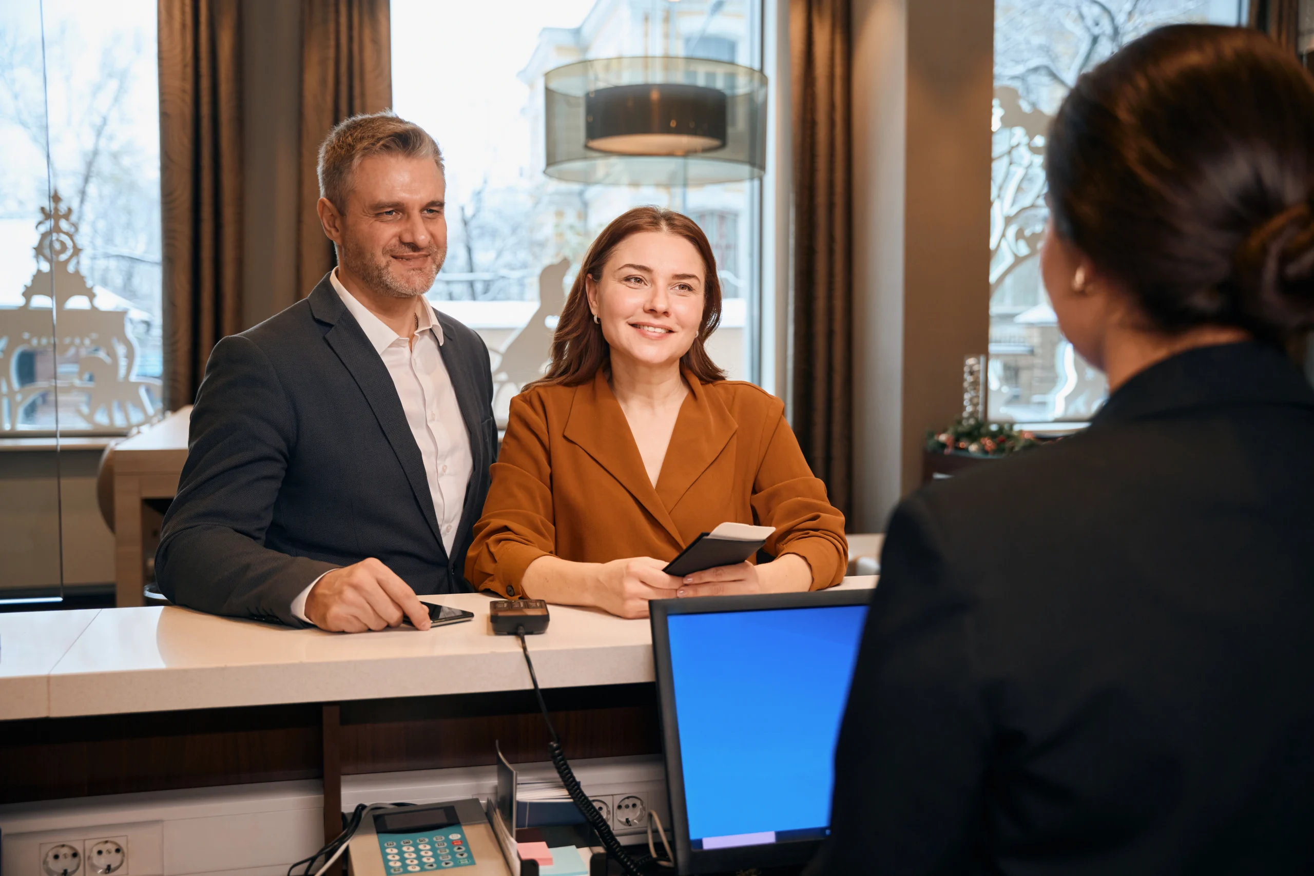 Couple looking at female reception desk during check-in in hotel lobby